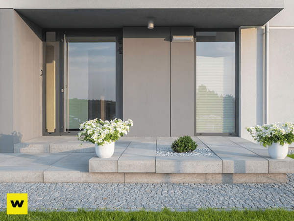 Moderner Hauseingang mit großen Glasflächen, Pflanzkübeln und gepflasterter Terrasse.